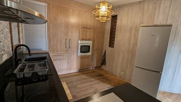 A kitchen with a black countertop, wooden cabinets, a built-in oven, a microwave, and a refrigerator.