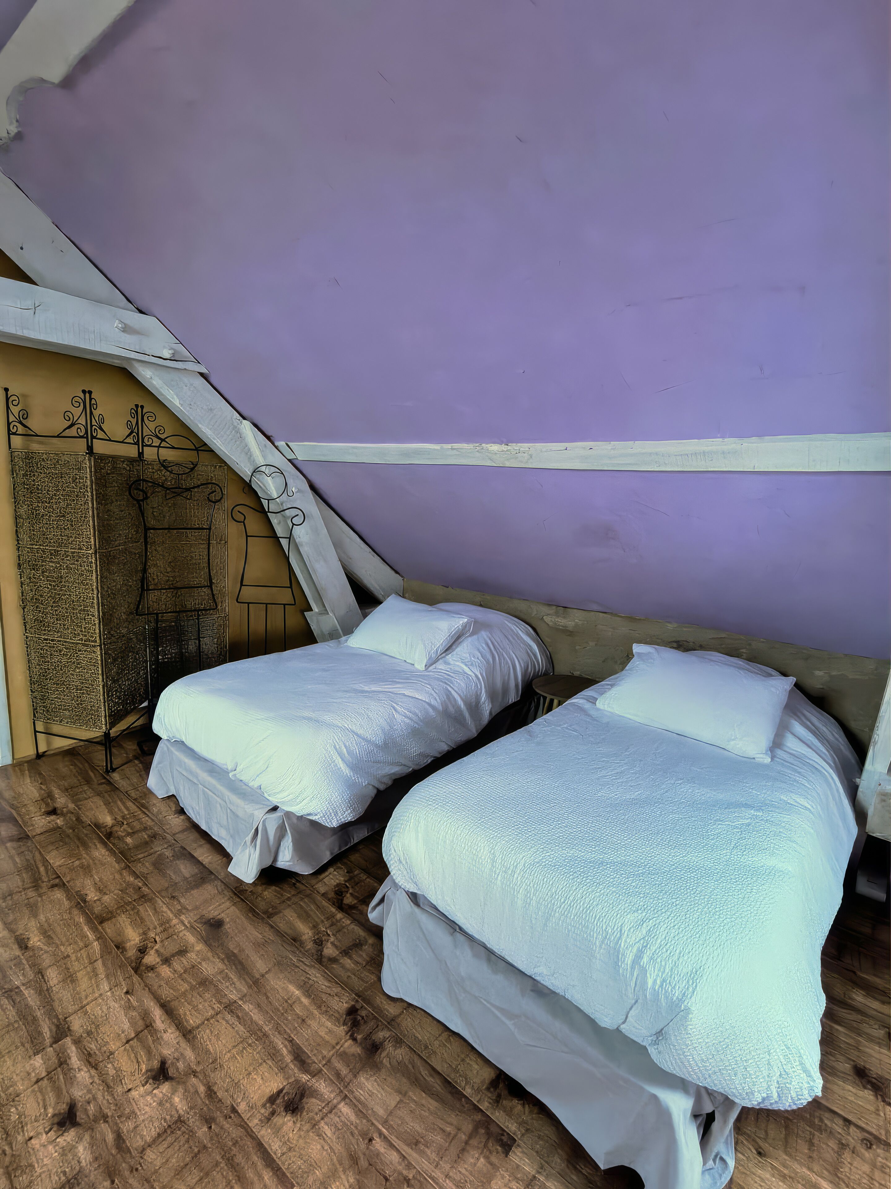 A room with two beds, wooden flooring, and a sloped ceiling.