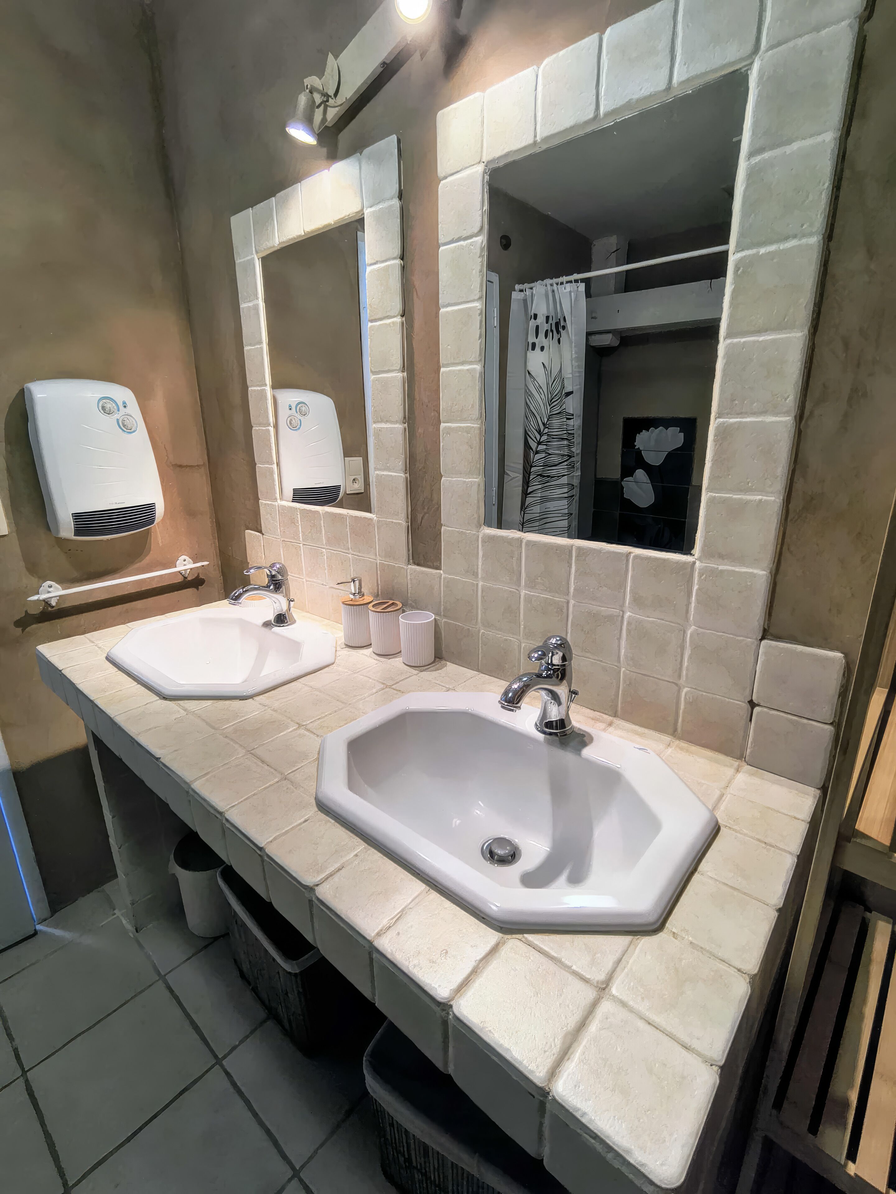 Baño con dos lavamanos, un secador de manos y un espejo.