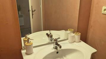 Une salle de bain avec un lavabo blanc, deux robinets, un miroir et trois articles de toilette rangés dans un porte-savon.