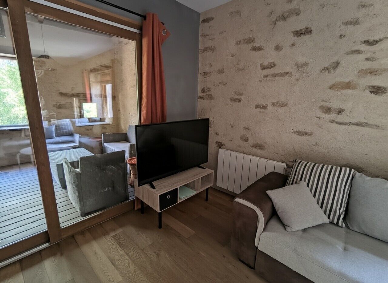 Una sala de estar con televisión, sofá y puerta corrediza de vidrio que da a un balcón.