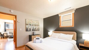 Ein Schlafzimmer mit einem Bett, Nachttischen, einem Wandbild und einem Fenster mit Jalousien.