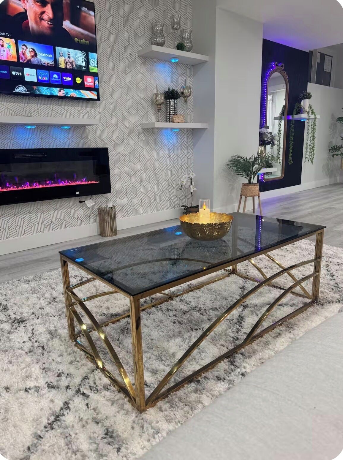Un salon moderne avec une table basse en verre, un téléviseur à écran plat fixé au mur et des étagères décoratives.