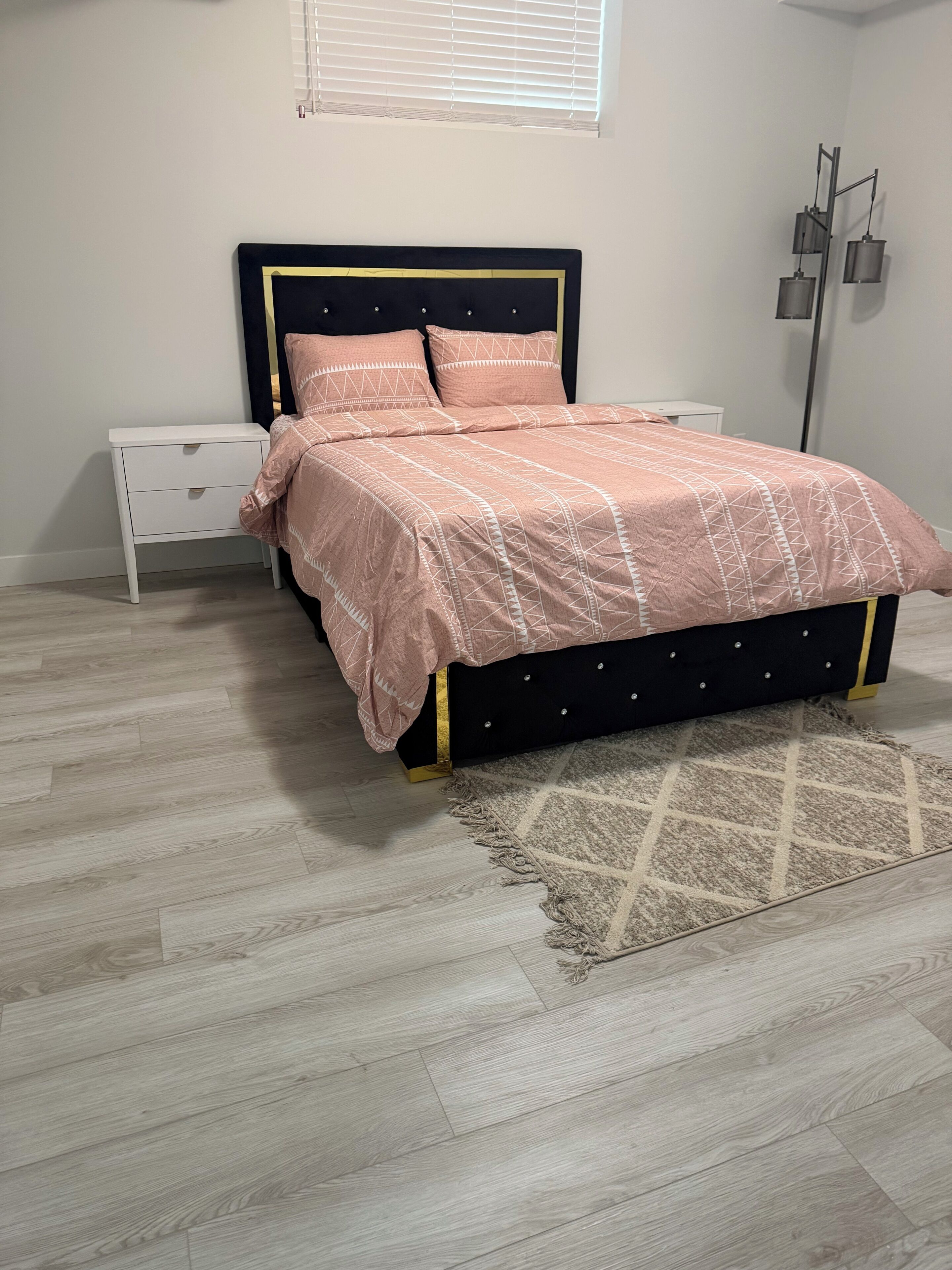 A bedroom with a bed, a nightstand, a floor lamp, and a window.