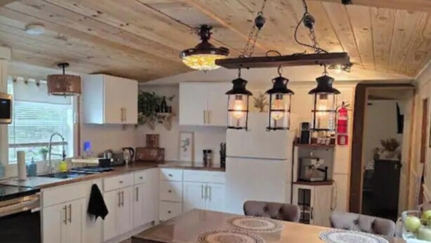 A kitchen with wooden cabinets, a dining table with chairs, pendant lights, and a refrigerator.