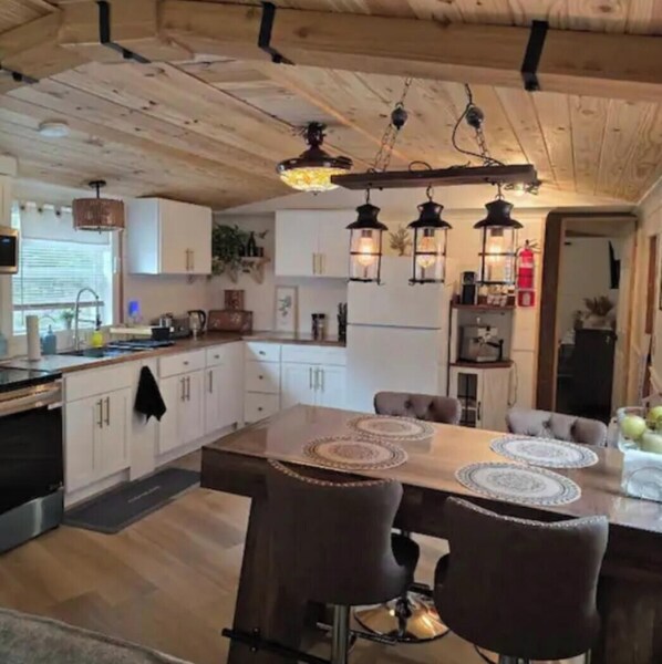 A kitchen with wooden cabinets, a dining table with chairs, pendant lights, and a refrigerator.