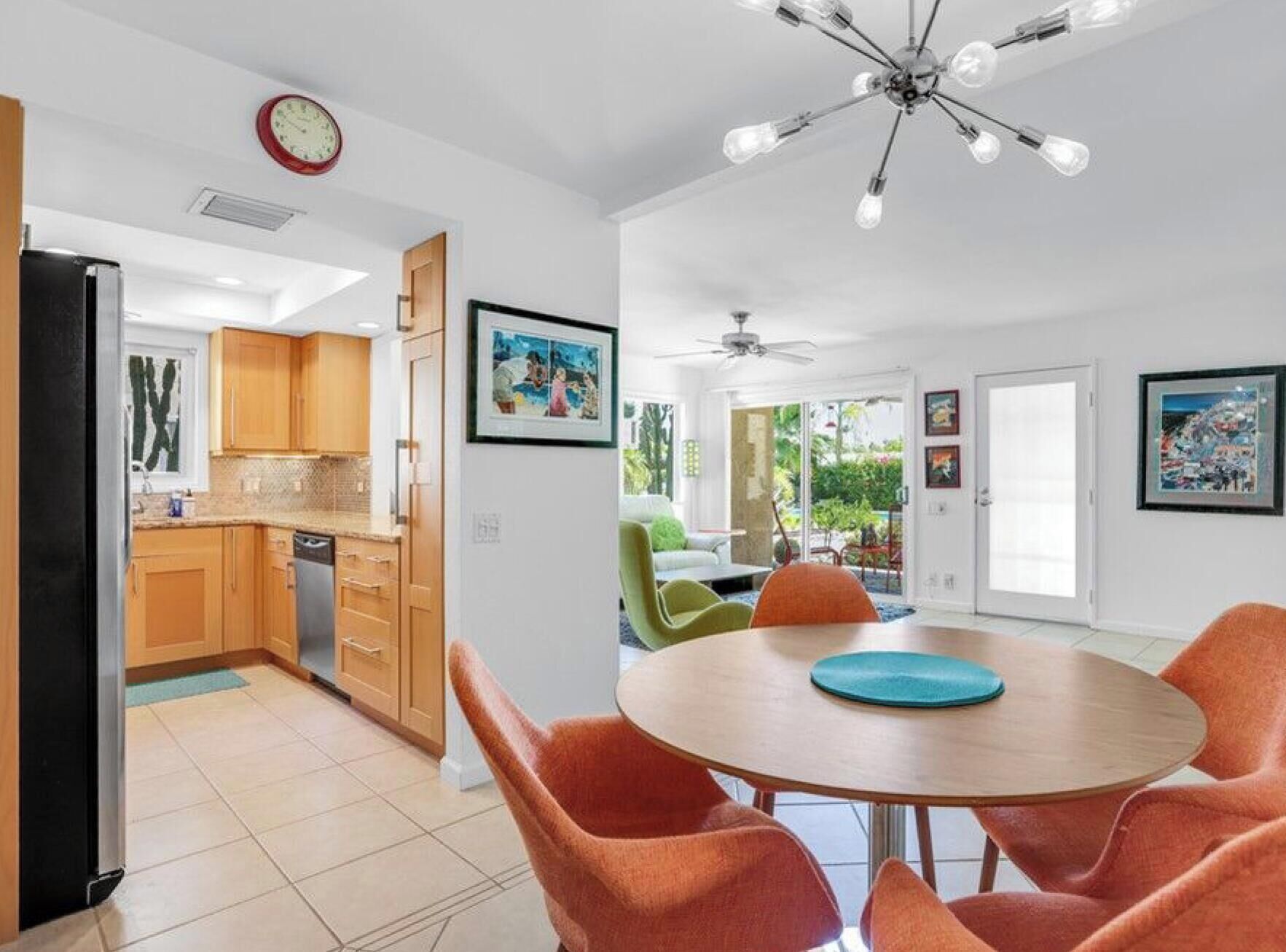 A modern kitchen with wooden cabinets, a dining area with orange chairs, and a ceiling fan.