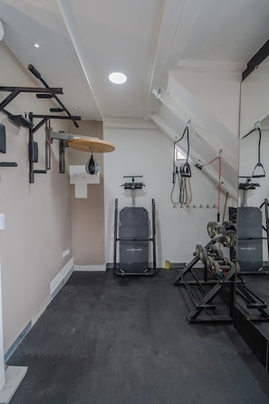 Uma academia com equipamentos de musculação, um saco de pancadas e um espelho.