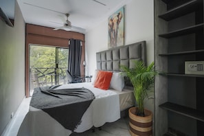 Quarto com cama grande, ventilador de teto, janela com cortinas, um quadro e um vaso de planta.
