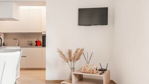 A modern kitchen with a flat-screen TV mounted on the wall, a small wooden side table with a vase of dried pampas grass, and a laptop.