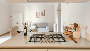 A modern kitchen with a gas stove, a dining area with a table and chairs, and a living room with a sofa and artwork on the wall.