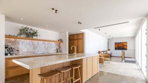 A modern kitchen with a large island, wooden bar stools, and a view of the living area. - Onetangi Estate including guest cottage by Waiheke Pure - Luxurious italian style palazzo with pool, hot tub and  expansive views (Onetangi)