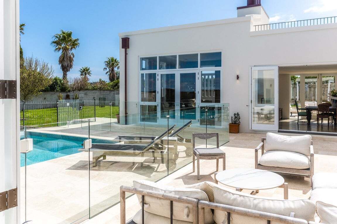 Une maison moderne dotée d’une piscine, d’un espace salon extérieur et d’une porte vitrée donnant sur un patio.