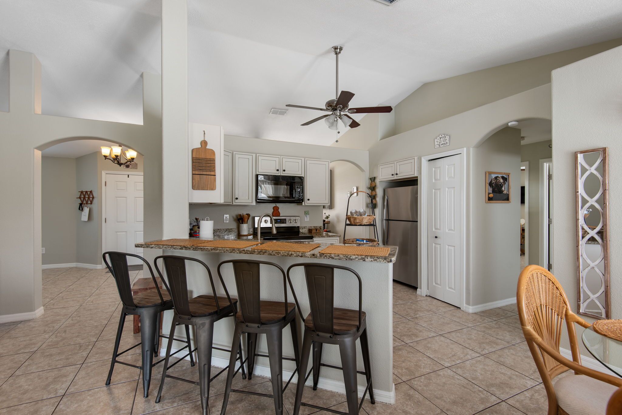 A modern kitchen with a central island, bar stools, and a ceiling fan.