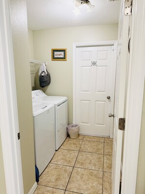 A laundry room with a washer and dryer, a trash can, and a door with a 'No Guest Access' sign.