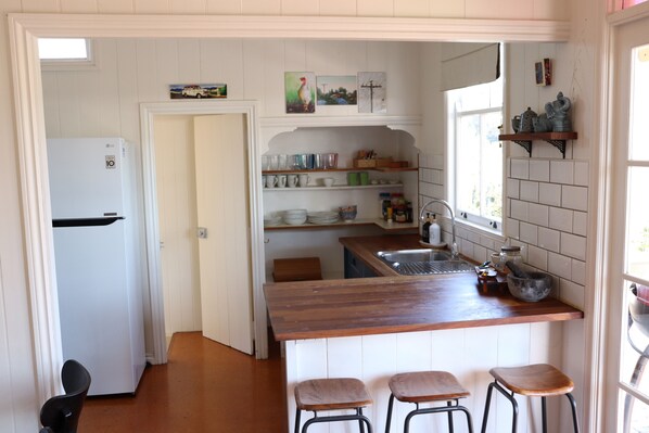 A kitchen with a wooden countertop, bar stools, a refrigerator, shelves with dishes, and a window. - Paddington Tower View Cottage (Red Hill)
