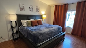 A bedroom with a bed, a ceiling fan, a nightstand, a lamp, and a window with curtains.