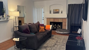 A living room with a sofa, a coffee table, a fireplace, and a ceiling fan.