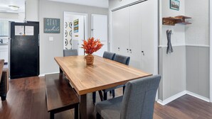 Un comedor con una mesa de madera, sillas tapizadas en gris y un jarrón con hojas anaranjadas.