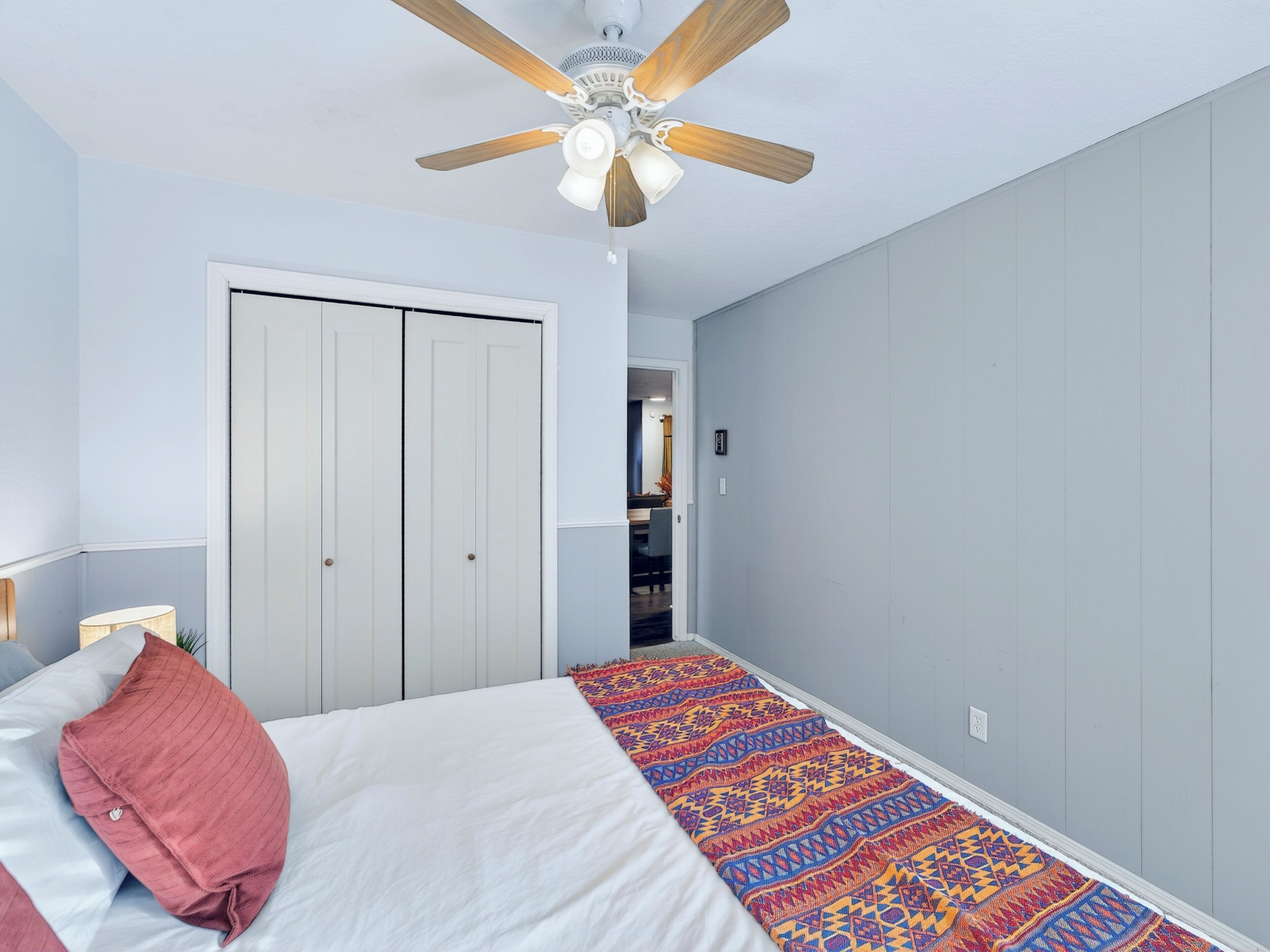 Une chambre à coucher avec un lit, un ventilateur de plafond, une porte et un tapis à motifs.