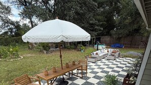 Un patio con piso a cuadros, mobiliario de madera y una sombrilla blanca.