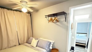 Un dormitorio con cama, ventilador de techo, estante con ropa y puerta que da a otra habitación.