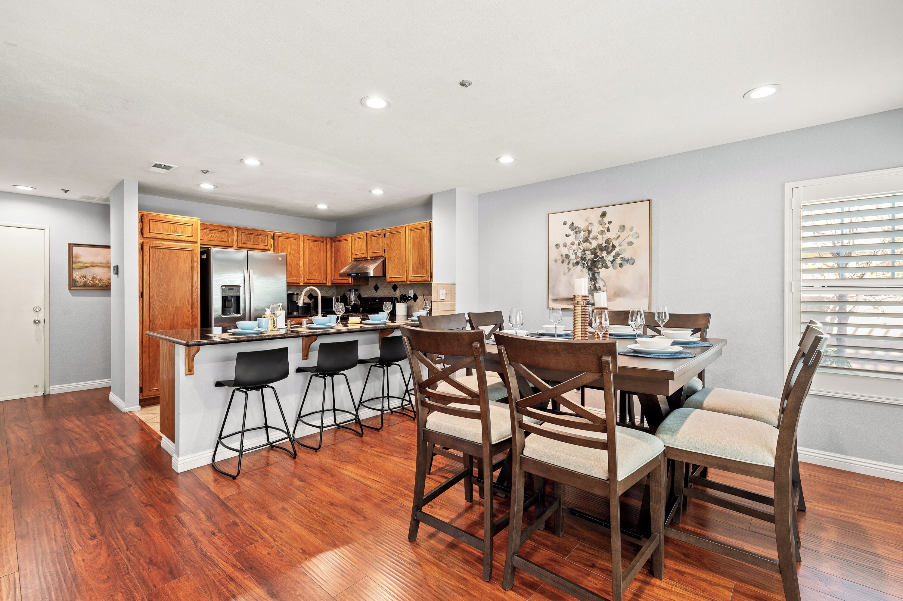 A modern kitchen with wooden cabinets, a stainless steel refrigerator, and a dining area with a table set for four.