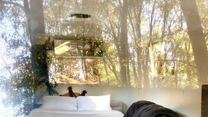 Un dormitorio con cama, mesita de noche y ventana con vistas a un bosque.