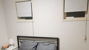 A bedroom with a bed, bedside table, lamp, and two windows with blinds. - Shared house with other guests near shopping center and theme park (Upper Coomera)