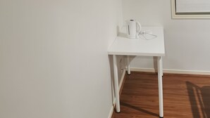 A white table with a kettle and a cup, a wooden cabinet above it, and a window with a white frame. - Shared house with other guests near shopping center and theme park (Upper Coomera)