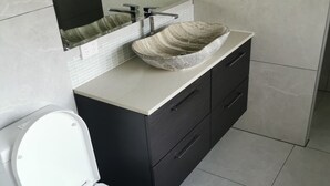 A modern bathroom with a white toilet, a large vessel sink, and dark cabinetry. - Shared house with other guests near shopping center and theme park (Upper Coomera)