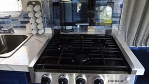 A kitchen with a stainless steel stove, a sink, and a window with a view of the outside.