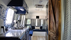 A compact RV kitchen with a sink, stove, and a window with curtains.