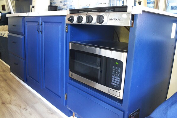 Een keuken met blauwe kastjes, een magnetron en een fornuis.
