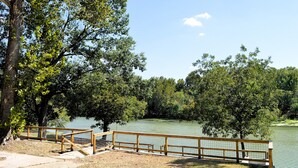 A wooden deck with a metal railing overlooking a calm lake, surrounded by dense trees.
