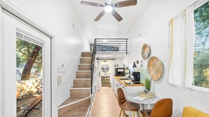 Un interior moderno con una escalera que lleva a una habitación en entrepiso, un comedor con vistas y una cocina con una pequeña isla.