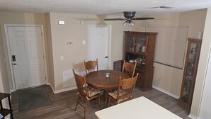 A dining room with a round table, four chairs, a ceiling fan, and a wooden cabinet with glass doors.