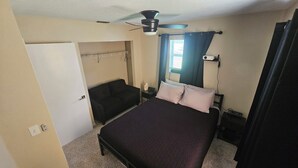 A bedroom with a bed, a chair, a wardrobe, a ceiling fan, and a window with curtains.