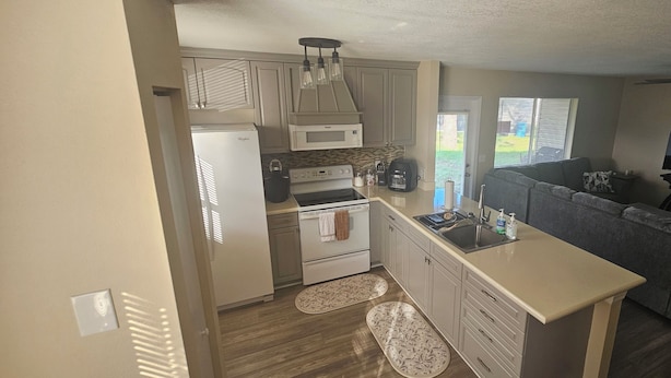 A kitchen with a refrigerator, stove, microwave, and sink. There is a wooden floor and a window with blinds.
