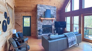 Ein Holzblockhaus-Innenraum mit Kamin aus Stein, einer Couch und einem Fernseher.