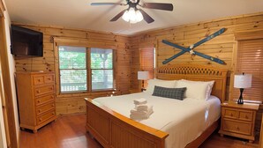 Ein Schlafzimmer mit Holzwänden, einem Bett, Nachttischen, einem Fernseher und einem Deckenventilator.