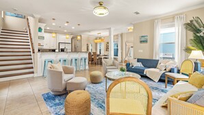 A spacious living room with a blue rug, a sofa, and a coffee table. There is a staircase leading to the upper floor. - Designer 5BR • Sleeps 14 • Dog OK + Pool-Hot Tub (Destin)