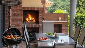Eine Terrasse im Freien mit Kamin aus Ziegelsteinen, Grill und Esstisch.