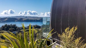 A modern building with a curved facade overlooking a lake and hills.