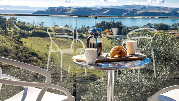 A balcony with a table set for breakfast, overlooking a scenic view of a lake and mountains.