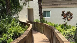 A wooden deck with railings, surrounded by greenery and a building in the background. - LUXE LOFT NAPLES (Naples)