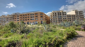 Un hôtel à plusieurs étages doté de balcons, entouré de verdure et bordé d’une promenade dallée.