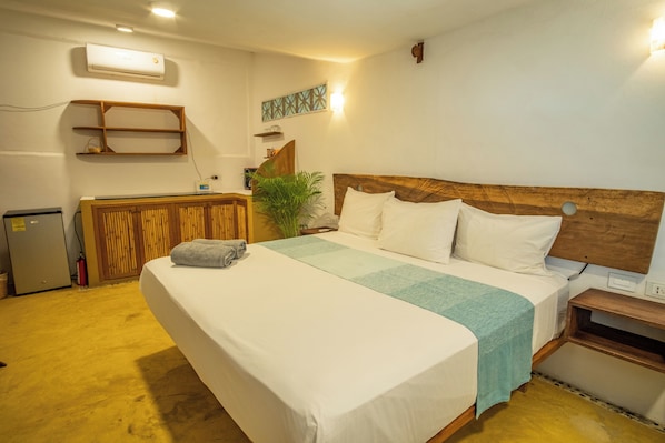 Habitación de hotel con una cama grande, cabecera de madera, un escritorio pequeño y un aire acondicionado montado en la pared.