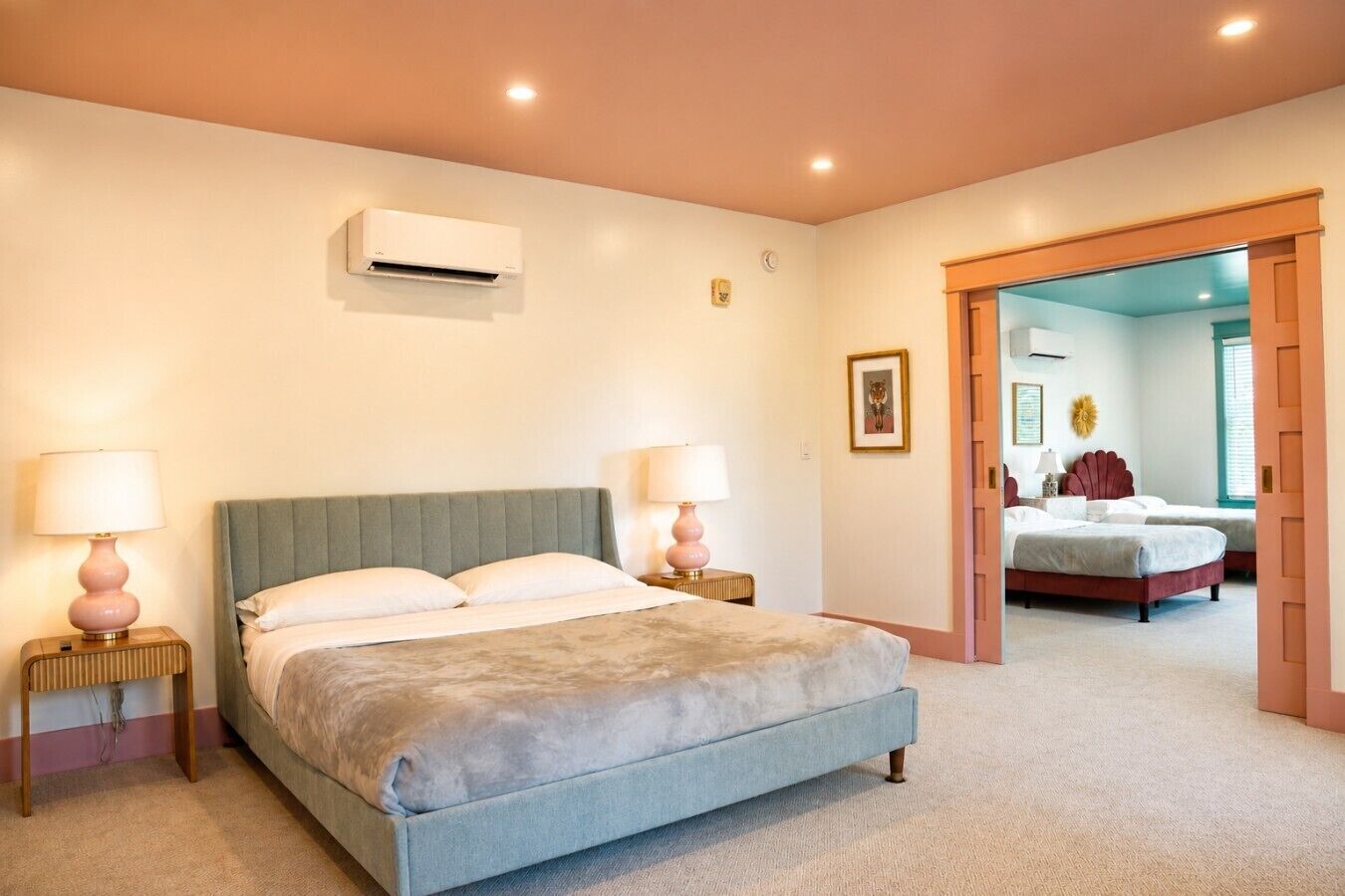Quarto com cama, luminárias de cabeceira, ar condicionado e uma porta que dá para outro cômodo.