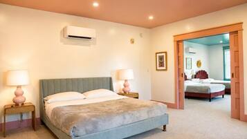 Quarto com cama, luminárias de cabeceira, ar condicionado e uma porta que dá para outro cômodo.